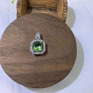 Detail view of cushion cut emerald green pendant with halo setting on a wood base