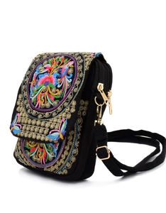 Detail view of ethnic floral embroidery on a black canvas crossbody bag with metal zippers
