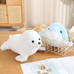 Niedliches Plüschtier-Set mit weißer Robbe und blauem Delfin auf Holztisch