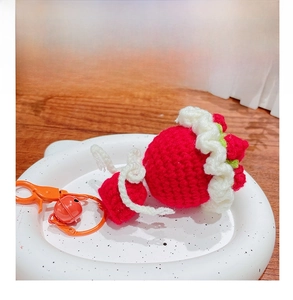 Detail of a handmade crocheted strawberry keychain with a green leaf and orange bell