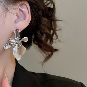 Close-up of a model wearing large silver metallic flower earrings with a polished finish