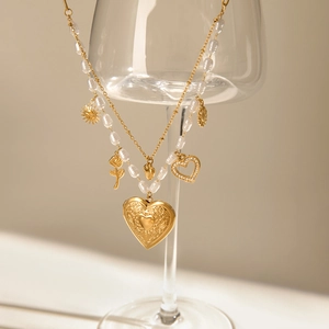 Gros plan d'un collier multicouche doré avec médaillon en cœur et perles blanches