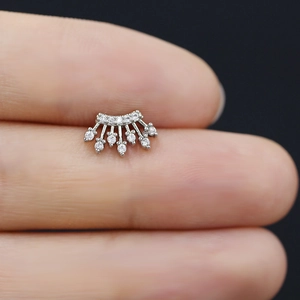 Dettaglio di un piercing a corona in argento con zirconi cubici tenuto in mano