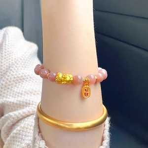 Detail of pink sunstone beaded bracelet with golden PiXiu and lucky charm on wrist