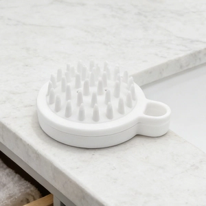 White silicone scalp massager brush placed on a marble surface for hair washing