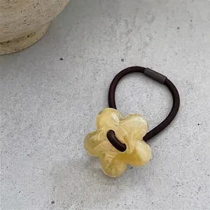 Close-up of yellow resin flower hair tie with dark brown elastic band on stone background