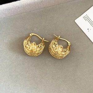 Macro shot of gold-plated hollow floral earrings on a textured grey background