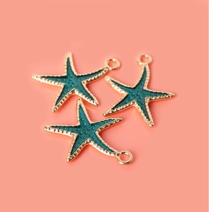 Detailed close-up of three starfish alloy pendants with turquoise enamel on pink background