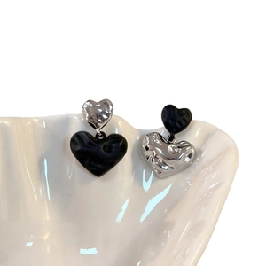 Asymmetric heart stud earrings with silver and black textured metal finish on a shell tray