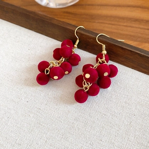 Detail of red velvet grape cluster earrings with gold hooks on a rustic wood stand