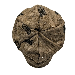 Detail of brown knitted beanie featuring black butterfly patterns and silver sequins