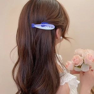 Close-up of a blue and purple fish-shaped hair clip worn on long hair for beach style