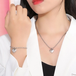 Ensemble collier pendentif coeur argenté et bracelet perlé porté par un mannequin en costume