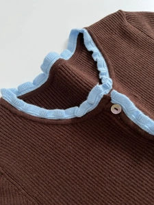 Close-up of ribbed knit top featuring a light blue ruffled collar and white button detail