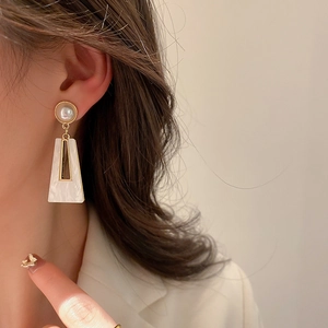 Close-up of geometric trapezoid earrings with white pearl and gold metal trim