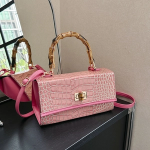 Detailed view of pink croc-effect handbag featuring a natural bamboo handle and gold lock