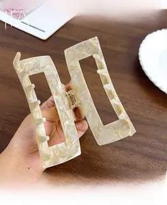 Close-up of a large square acetate hair claw clip with cream marble pattern and metal spring