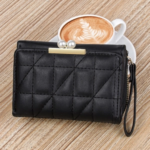 Close-up of black quilted wallet with pearl gold clasp on a wooden table with coffee