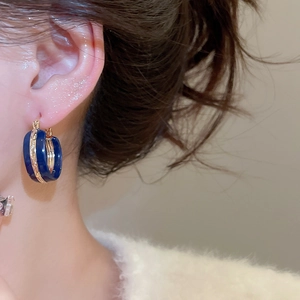 Close-up of deep blue enamel earring with gold-tone accents worn by a model