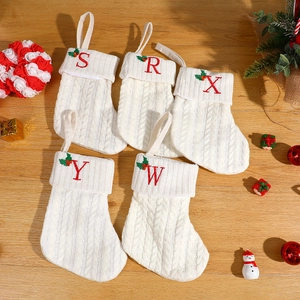 White knit Christmas stockings with red embroidered letters on a festive wooden table