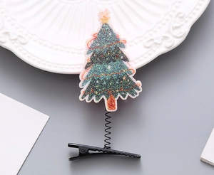 Detailansicht einer grünen Glitzer-Weihnachtsbaum-Haarklammer mit Feder auf grauem Grund