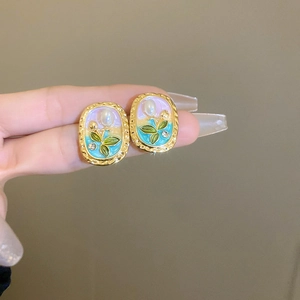 Detail of vintage enamel flower earring with pearl inlay and floral pattern on hand