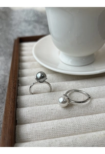 Dettaglio di anelli con perle in argento S925 grigie e bianche su espositore classico