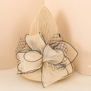 Detail of beige straw beach hat featuring large organza bow and black mesh decor