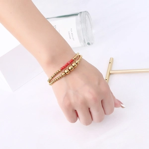 Close-up of stacked gold stainless steel beads and faceted red crystal elastic bracelets