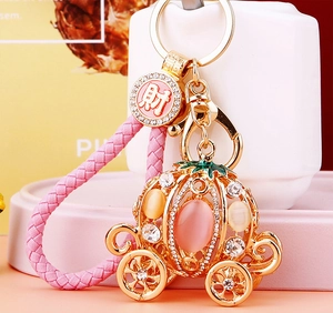 Close-up of golden pumpkin carriage keychain with pink cat eye stone and crystal details