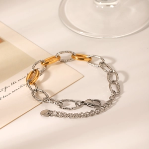 Detail of two-tone gold and silver chain bracelet with lobster clasp on a modern desk