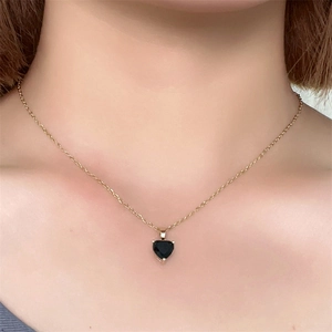 Close-up of a gold heart pendant necklace with black zircon worn on a person