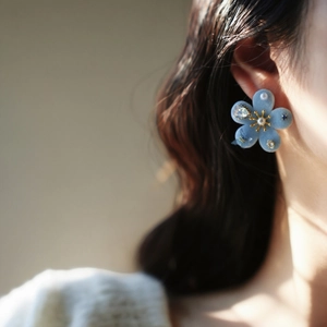 Close-up detail of blue flocked flower pearl stud earring with zircon worn on ear