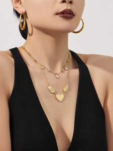 Detailed view of model wearing gold layered necklace with heart wing and floral pendants