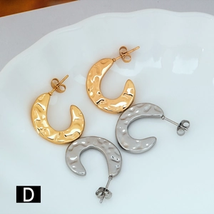 Detail of C-shaped hammered texture earrings in gold and silver finish on white tray