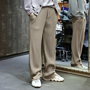 Detail of khaki pleated men's trousers featuring drawstring waist and textured fabric