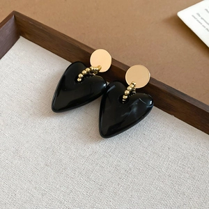 Detail shot of heart-shaped black acrylic earrings with gold beads on grey textured cloth
