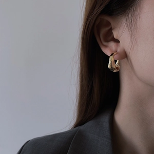 Close-up of golden textured geometric earrings worn with a charcoal gray suit