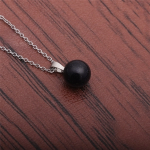 Close-up of minimalist black stone round pendant on a silver necklace over wood background