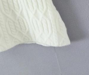Close-up of white knitted long sleeve dress showing detailed cable knit texture and pattern