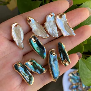 Handheld view of natural baroque pearl and abalone shell pendants with gold plated edges