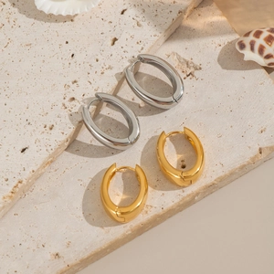Elegant gold and silver U-shaped hoop earrings on a stone surface with seashells