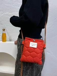 Close-up of orange quilted nylon crossbody bag with woven rope strap and brand label