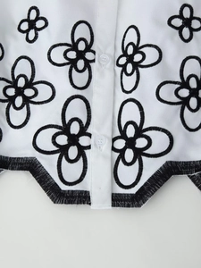 Close-up of white shirt featuring black floral embroidery and scallop hem details