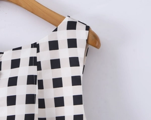 Close-up of sleeveless plaid dress on wooden hanger showing fabric texture and check pattern