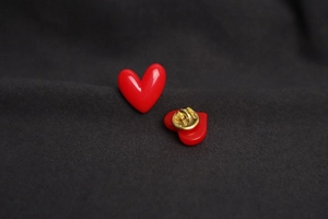 Detailed view of red heart brooch with golden butterfly clutch back on grey fabric