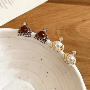 Detailed close-up of crown earrings with pearls and gemstones on a wooden surface