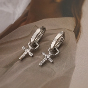 Silver hoop earrings with sparkling zircon cross pendants on soft fabric background