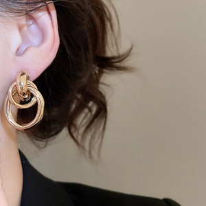 Close-up of golden multi-layered geometric hoop earrings worn by a model in a luxury style