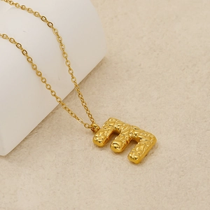 Detailed macro of golden letter E pendant with unique hammered metal texture and O-chain